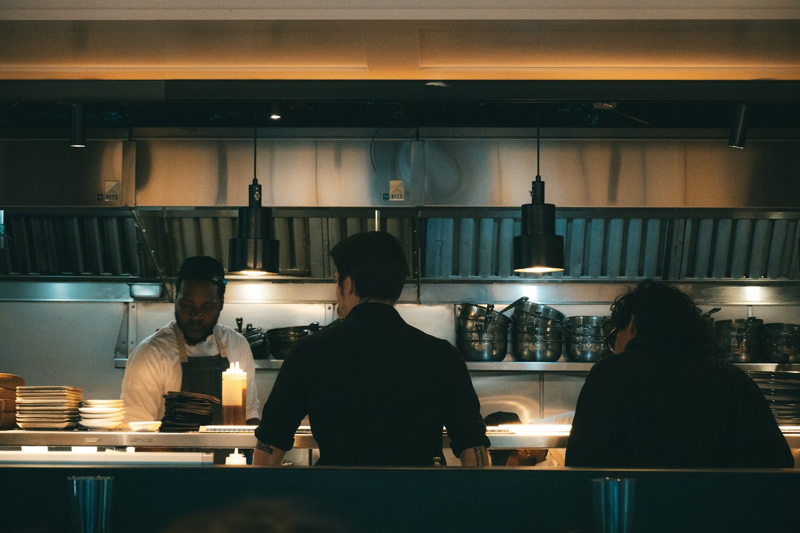 Photo by Willian Justen de Vasconcellos Chefs prepare food in a dimly lit restaurant.